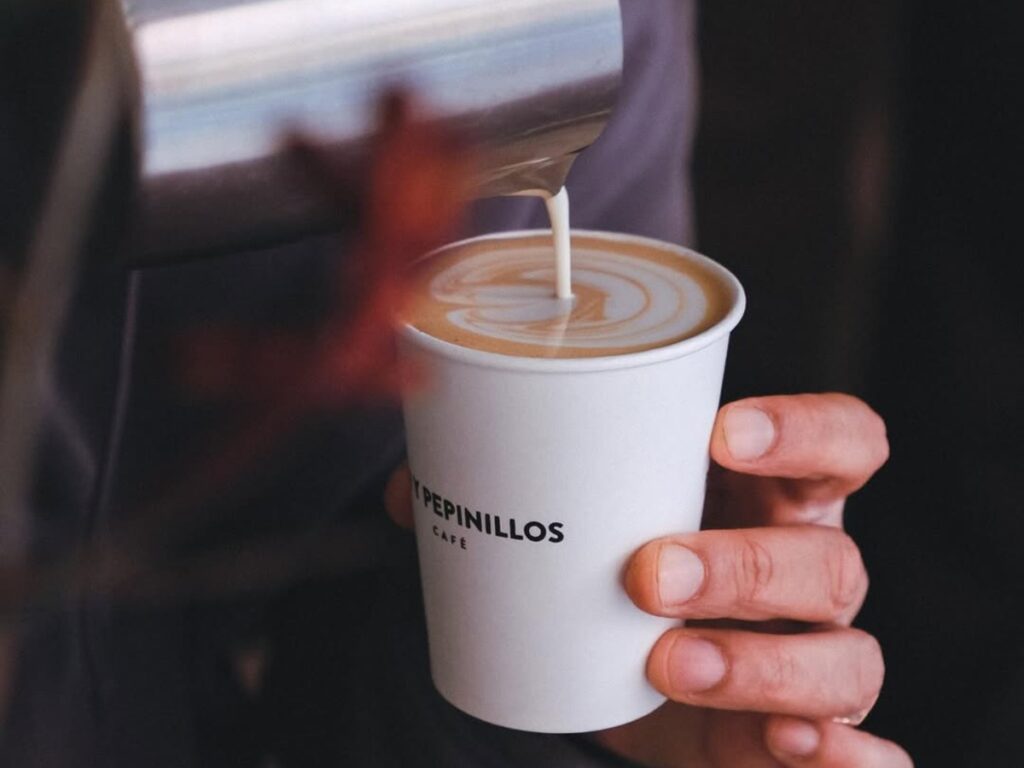 specialty-coffee-pour-latte-art-malasana-madrid-pan-y-pepinillos-cafe Barista pouring milk into a takeaway cup at Pan y Pepinillos Café, specialty coffee shop in Madrid